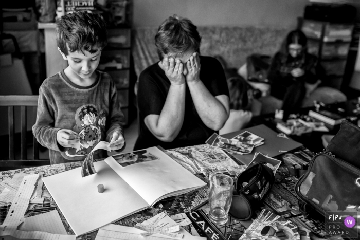 Photo by: <a href="https://www.fpja.com/documentary-family-photography-contests/maryline-krynicki/%C3%AEle-de-france/2077571">Maryline Krynicki - France</a> A mother covers her eyes as her son helps put a scrap book together in this Family Photojournalist Association award-winning photo by a France documentary family photographer.