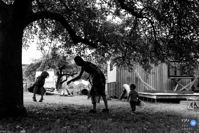 A mother pushes her daughter on a tire swing hanging from a large tree in this black and white photograph by a Netherlands family photojournalist. 