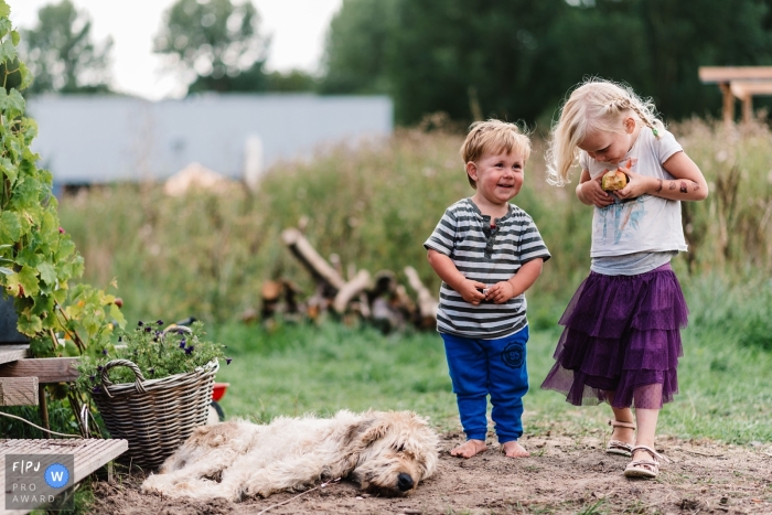 Un garçon et une fille marchent ensemble à l'extérieur alors qu'un chien se couche par terre devant eux sur cette photo réalisée par un photojournaliste de famille du Gueldre, Pays-Bas.