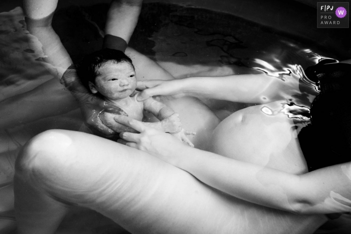 Une mère et une infirmière tiennent un nouveau-né dans une baignoire d'accouchement juste après une naissance dans l'eau, sur cette photo en noir et blanc réalisée par un photographe de naissance de Groningue, aux Pays-Bas.