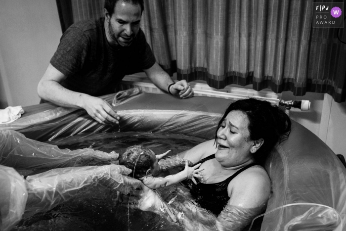 Photo by: <a href="https://www.fpja.com/documentary-family-photography-contests/marjolein-roossien/groningen/2077876">Marjolein Roossien - Netherlands</a> A nurse hands a mother her baby to hold for the first time in the birthing tub after her water birth in this black and white image by a Groningen, NL birthing photographer.