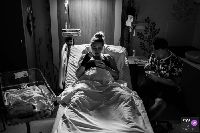 Photo by: <a href="https://www.fpja.com/documentary-family-photography-contests/marjolein-roossien/groningen/2077886">Marjolein Roossien - Netherlands</a> A mother and father sit in a hospital room eating as their newborn sits next to them in this black and white photo by a Groningen, Netherlands birth photographer.