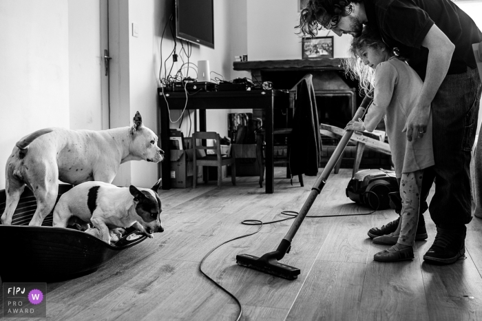Photo by: <a href="https://www.fpja.com/documentary-family-photography-contests/nadine-court/savoie/2077986">Nadine Court - France</a> Two dogs get upset and hide in their bed as a little girl and her father vaccuum the floor in this black and white photo by an Auvergne-Rhone-Alpes family photographer
