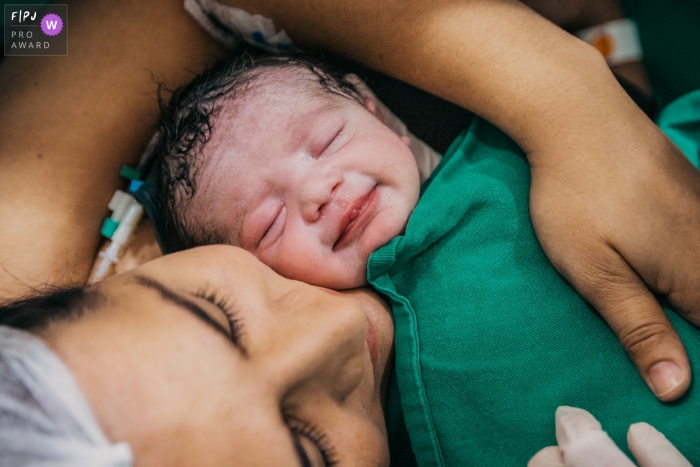 A mother cradles her sleeping newborn for the first time in the hospital in this image by a Manaus birthing photographer.