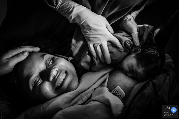 Photo by: <a href="https://www.fpja.com/documentary-family-photography-contests/anne-lucy-silva-barbosa/manaus/2078466">Anne Lucy Silva Barbosa - Brazil</a> A doctor helps a baby nurse for the first time in the hospital as the mother smiles in this black and white photo by a Manaus birth photographer.