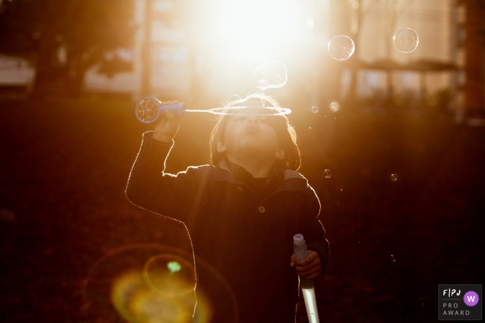 A child blows bubbles outside surrounded by sunlight in this photo by a Rio Grande do Sul, Brazil documentary-style family photographer.