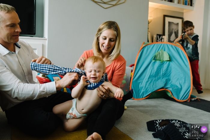 Photo by: <a href="https://www.fpja.com/documentary-family-photography-contests/claire-batey/northumberland/2079121">Claire Batey - United Kingdom</a> A mother and father try to dress their baby boy in this photo by a Northumberland, England, UK family photographer