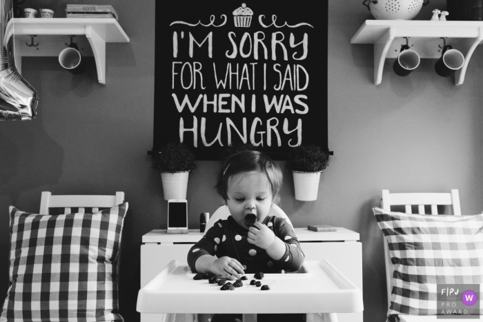 A little girl sits in her high chair eating berries in this black and white photo by a Northumberland, England documentary-style family photographer.