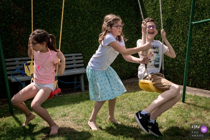 Photo by: <a href="https://www.fpja.com/documentary-family-photography-contests/sybil-rondeau/nantes/2079366">Sybil Rondeau - France</a> Three children play on a swing set outside in this photo by a Nantes family photographer.