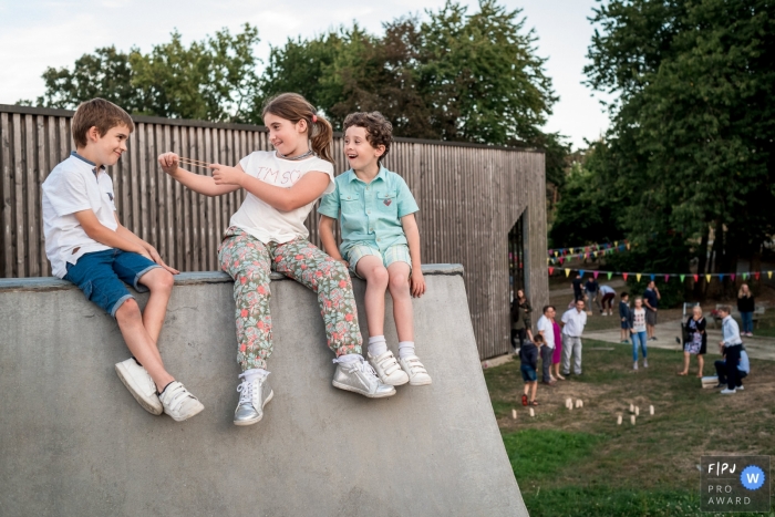 Trois enfants sont assis sur une rampe de planche à roulettes pendant que la petite fille feint de lancer un élastique à l'un des garçons dans cette image primée du FPJA par un photographe de la famille nantaise.