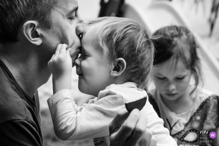 Photo by: <a href="https://www.fpja.com/documentary-family-photography-contests/annie-gozard/paris/2079656">Annie Gozard - France</a> A little boy pinches his father's cheeks as he kisses the boy's forehead in this black and white photo by a Paris, France family photojournalist.