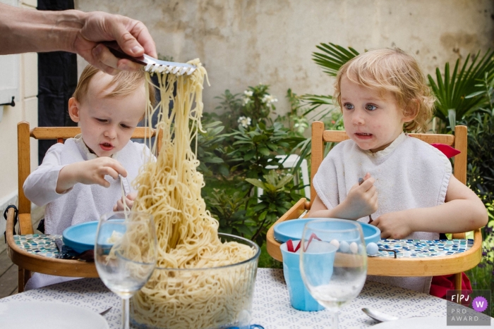 Photo by: <a href="https://www.fpja.com/documentary-family-photography-contests/annie-gozard/paris/2079991">Annie Gozard - France</a> Two children wait eagerly in their high chairs as their father scoops pasta from a bowl in this winning picture by a Paris, France family photojournalist.