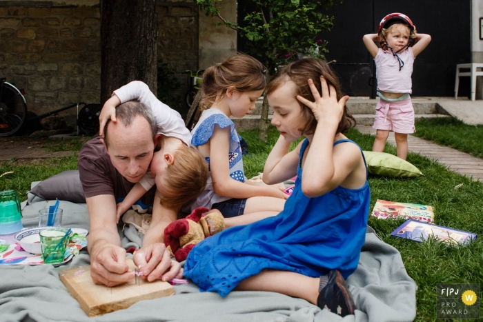 Photo by: <a href="https://www.fpja.com/documentary-family-photography-contests/annie-gozard/paris/2080001">Annie Gozard - France</a> Paris family photojournalist captured this photo of a father enjoying a picnic with his children in the yard
