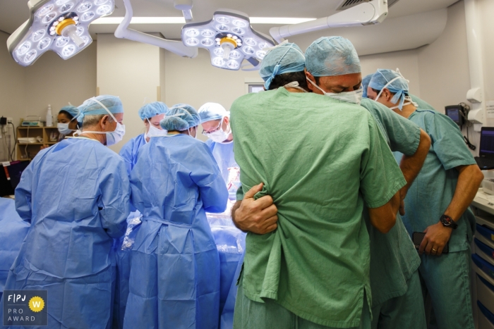 São Paulo hospital birth photographer captured this photo of two men in scrubs hugging while a hospital team operates in the background