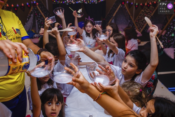 Plusieurs enfants lèvent leurs tasses pour se rafraîchir, assis autour de la table sur cette image photographique réalisée par un photojournaliste de famille à Sao Paulo, Brésil.