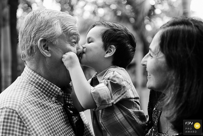 This black and white documentary family photograph of a toddler kissing his grandfather on the nose was captured by a 	Rio Grande do Sul photographer