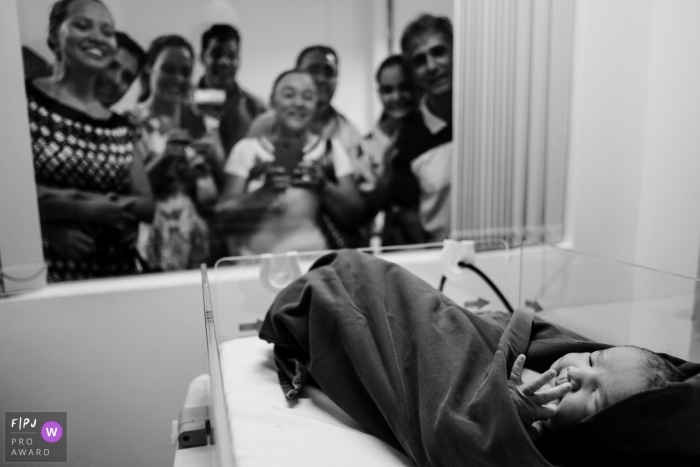 Photo by: <a href="https://www.fpja.com/documentary-family-photography-contests/emanuelle-rigoni/recife/2080301">Emanuelle Rigoni - Brazil</a> Family members look through the hospital window at their newest family member in this black and white photo by a Recife, Pernambuco birth photographer.