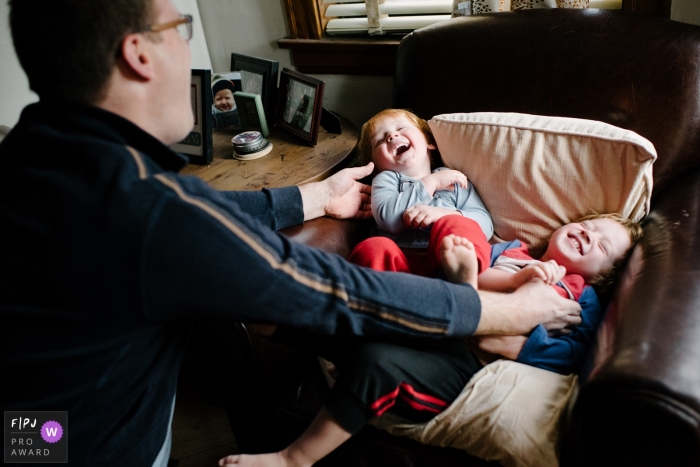 Photo by: <a href="https://www.fpja.com/documentary-family-photography-contests/laurie-peacock/chicago/2080551">Laurie Peacock - United States</a> Two little boys laugh as their father tickles them in this photo recorded by a Chicago, IL award-winning, documentary-style family photographer.