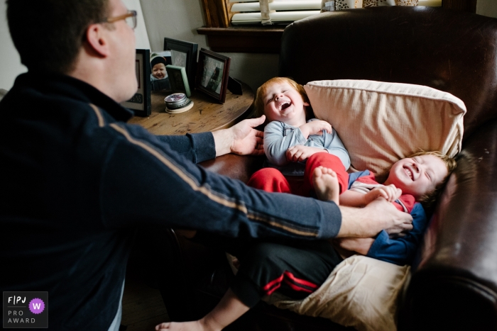 Two little boys laugh as their father tickles them in this photo recorded by a Chicago, IL award-winning, documentary-style family photographer. 