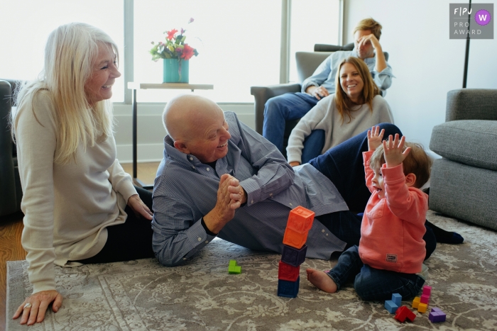 Les grands-parents sont assis par terre et regardent leur petite-fille jouer avec les blocs de construction de cette photo réalisée par un photographe de famille documentaire de Chicago, IL.