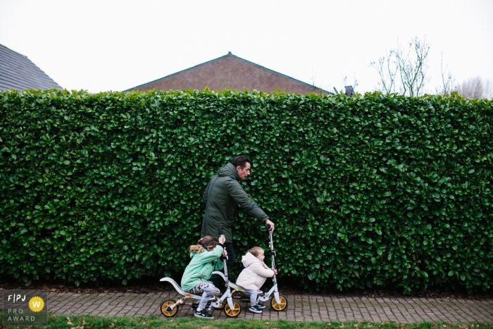 Zuid Holland documentary family photographer captured this photo of a father leading two young children down the street on their bikes