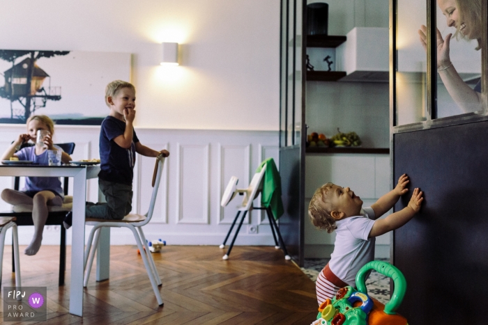 Photo by: <a href="https://www.fpja.com/documentary-family-photography-contests/marine-poron/paris/2081316">Marine Poron - France</a> A little boy looks up at his mother behind a window in the kitchen in this photograph created by a Paris, France family photojournalist.
