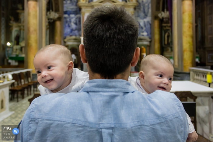 Two babies look over their father's shoulder as he holds them in a church in this documentary-style family image recorded by a Sao Paulo, Brazil photographer. 