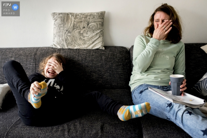 A mother and daughter laugh together on a couch in this FPJA award-winning picture by a Netherlands family photographer.