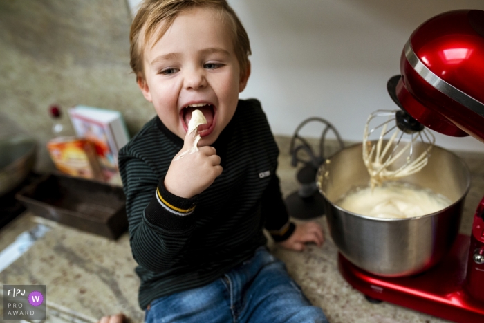 Photo by: <a href="https://www.fpja.com/documentary-family-photography-contests/gonda-meurs/noord-holland/2081526">Gonda Meurs - Netherlands</a> A boy licks batter off his finger as he sits next to the mixer in this FPJA award-winning image captured by a Holland family photographer.