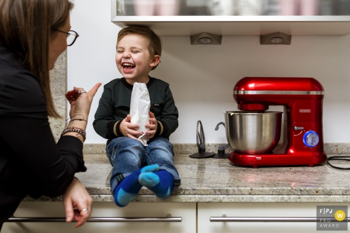 Photo by: <a href="https://www.fpja.com/documentary-family-photography-contests/gonda-meurs/noord-holland/2081571">Gonda Meurs - Netherlands</a> Noord Holland family photojournalist captured this image of a happy toddler sitting on the kitchen counter while holding a bag of treats