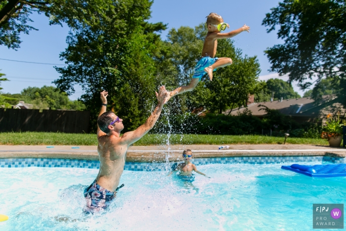 A father throws his sun in the air in a pool in this family picture by an Overland Park, KS photographer. 