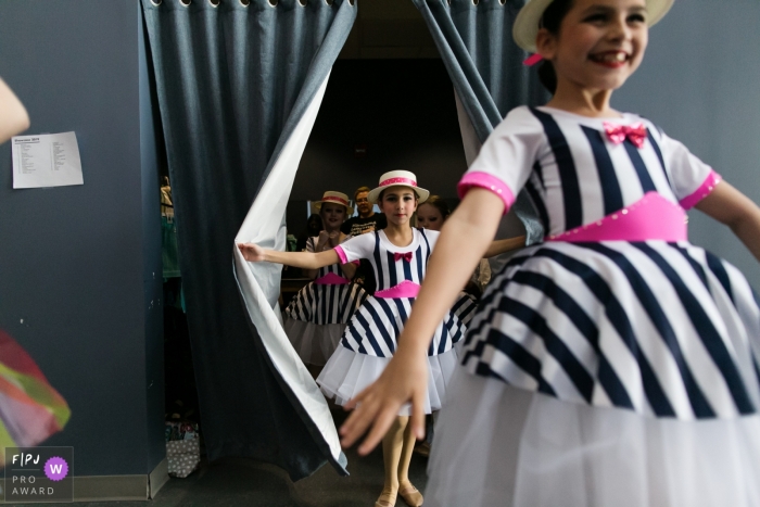 Girls in striped dresses emerge from behind a curtain in this photograph by an Overland Park, KS documentary family photographer. 