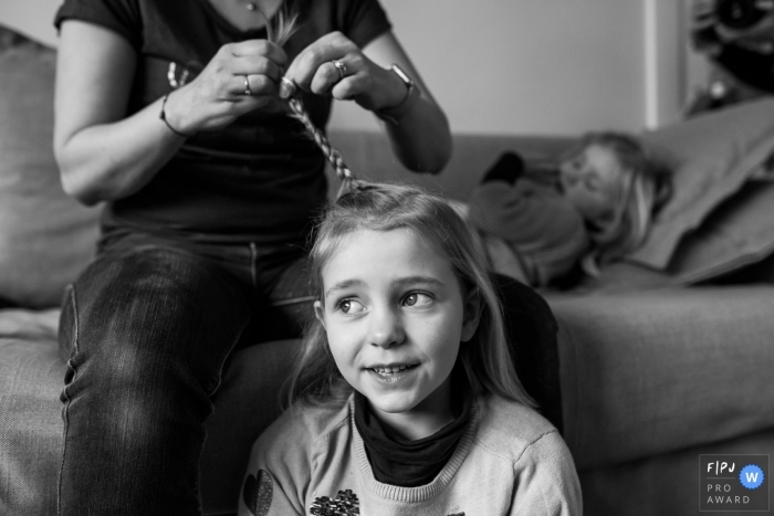 A mother braids her daughter's hair in this black and white reportage photograph by a Surrey, England family photojournalist. 