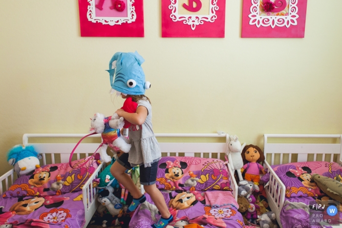 A little girl jumps on her bed with a toy fish on her head in this FPJA award-winning image captured by a Phoenix, AZ family photographer. 