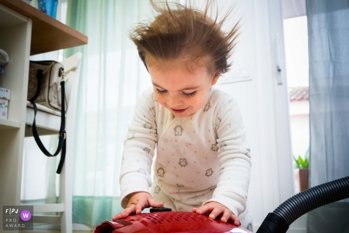 Photo by: <a href="https://www.fpja.com/documentary-family-photography-contests/antonio-calatayud/valencia/2083216">Antonio Calatayud - Spain</a> A little girl's hair blows back as she stands over a vacuum in this photo recorded by a Valencia, Spain award-winning, documentary-style family photographer.