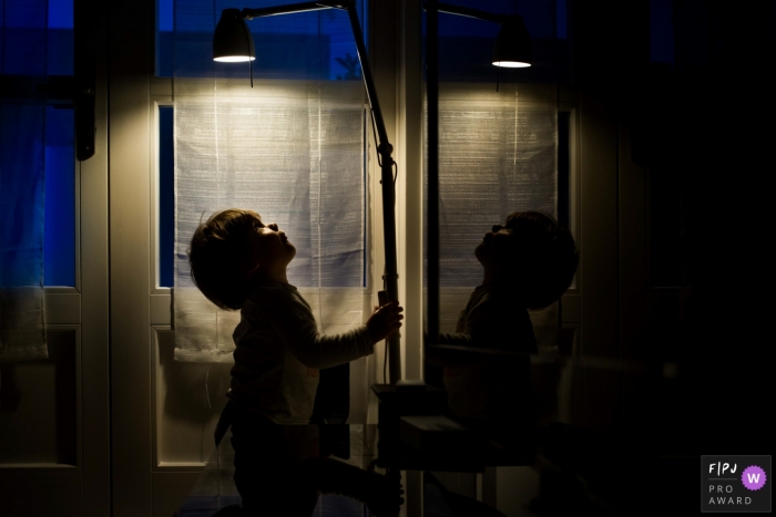 Un garçon joue avec une lampe dans une pièce sombre sur cette image prise par un photojournaliste de famille à Valence, en Espagne.