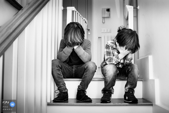 Two boys sit on the stairs covering their faces in this photo by a Valencia, Spain award-winning family photographer. 