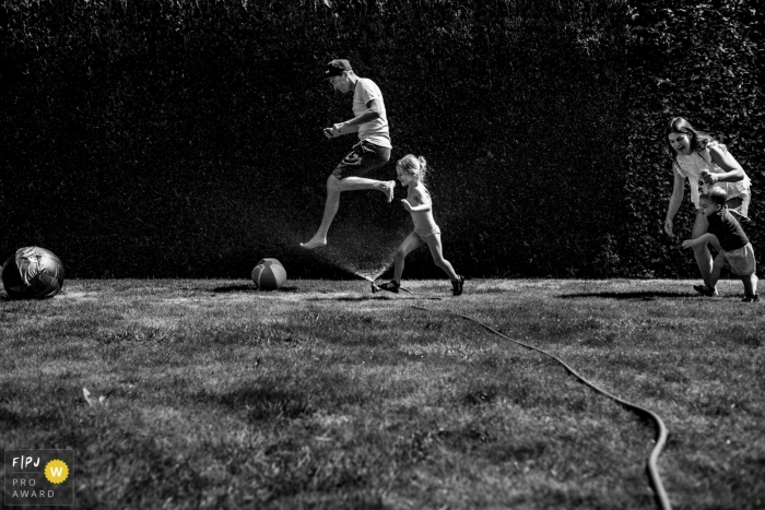 Photo by: <a href="https://www.fpja.com/documentary-family-photography-contests/marieke-zentjens/eindhoven/2083336">Marieke Zentjens - Netherlands</a> Eindhoven documentary family photographer captured this black and white photo of a family of four running through a sprinkler in their yard
