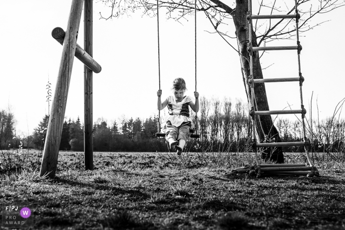 Photo by: <a href="https://www.fpja.com/documentary-family-photography-contests/marieke-zentjens/eindhoven/2083376">Marieke Zentjens - Netherlands</a> A little girl plays on a swing set outside in this black and white photo by an Eindhoven reportage family photographer.