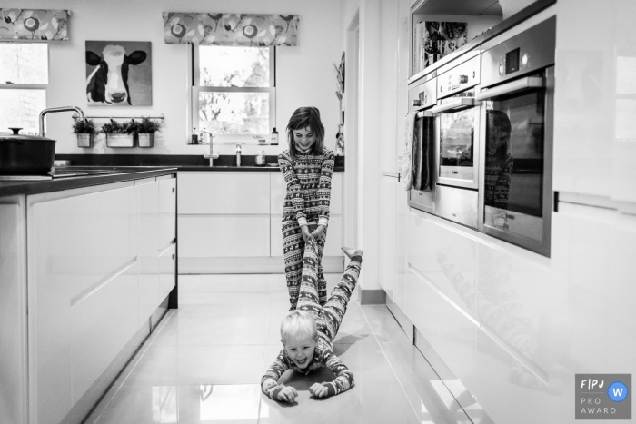 Photo by: <a href="https://www.fpja.com/documentary-family-photography-contests/alice-chapman/cambridgeshire/2083496">Alice Chapman - United Kingdom</a> A girl pulls her brother along a tile floor in this black and white photo by a Cambridgeshire, English reportage family photographer.