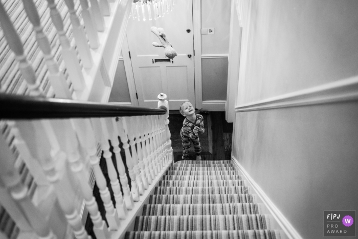 Un petit garçon jette son ours en l'air au bas de l'escalier sur cette photo en noir et blanc d'un photographe de famille du Cambridgeshire, style de reportage anglais.