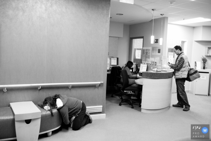 A man works on getting his wife checked into the hospital in this black and white photo by a Virginia award-winning birthing photographer. 