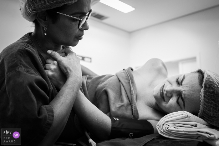 A nurse tries to comfort a woman giving birth in the hospital by holding her hand in this black and white image recorded by a Minas Gerais, Brazil family photographer