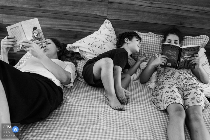 Two women sit in bed reading with a little boy between them in this award-winning photo by a Minas Gerais documentary family photographer.