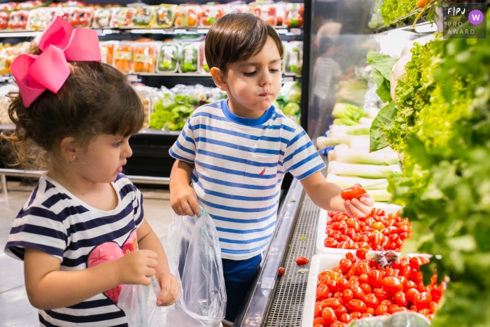 A girl and boy pick out tomatoes at the grocery store in this FPJA award-winning image captured by a Minas Gerais family photographer. 