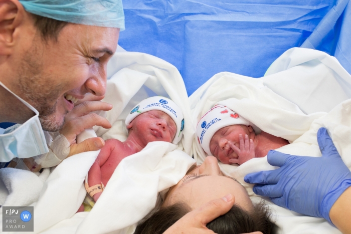 A father and mother hold their newborn twins in the hospital in this photograph captured by a Sao Paulo, Brazil birthing photographer. 