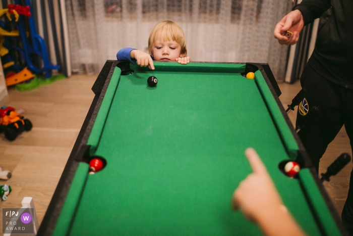 Un petit garçon tente de toucher une balle de billard sur une table de billard miniature sur cette photo réalisée par un photojournaliste de famille à Saint-Pétersbourg, Russie