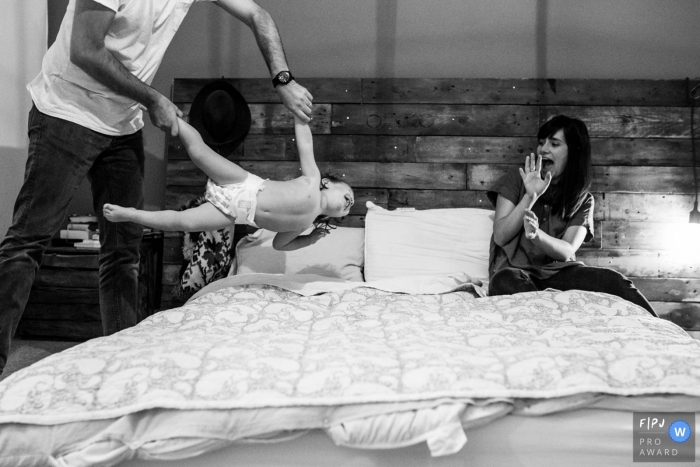 A father tosses his son onto a bed as his mother shields herself in this documentary-style family photo captured by a Essex, England photographer. 