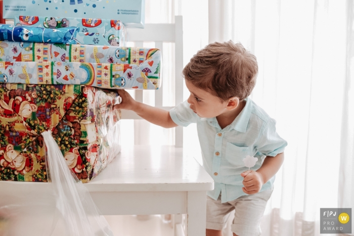 Photo by: <a href="https://www.fpja.com/documentary-family-photography-contests/thiago-braga/florianopolis/2085241">Thiago Braga - Brazil</a> Florianopolis family photojournalist captured this photo of a curious toddler checking out a stack of wrapped presents