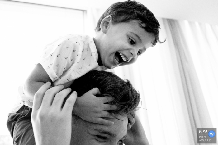 A little boy holds onto his father's head as he rides on his shoulders in this Family Photojournalist Association awarded photo by a Santa Catarina documentary family photographer.